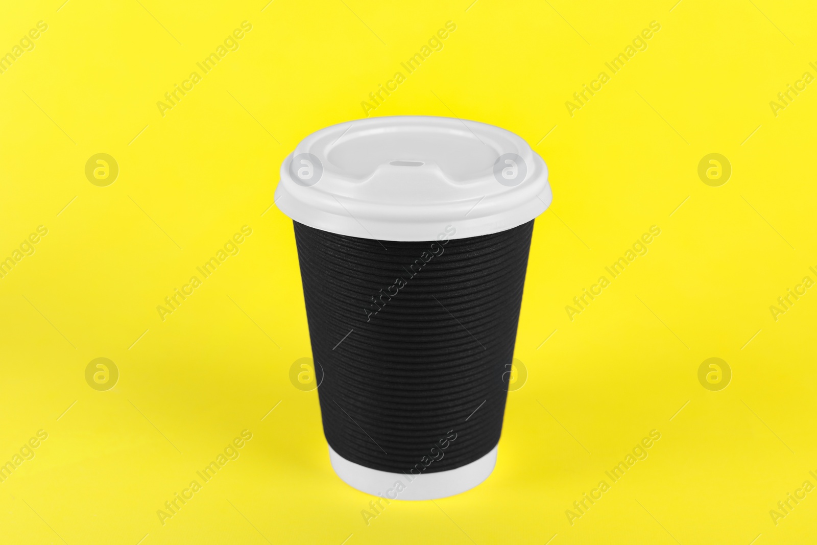 Photo of Black paper cup with plastic lid on yellow background. Coffee to go