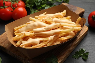 Tasty potato fries, cheese sauce in paper container and products on black table, closeup