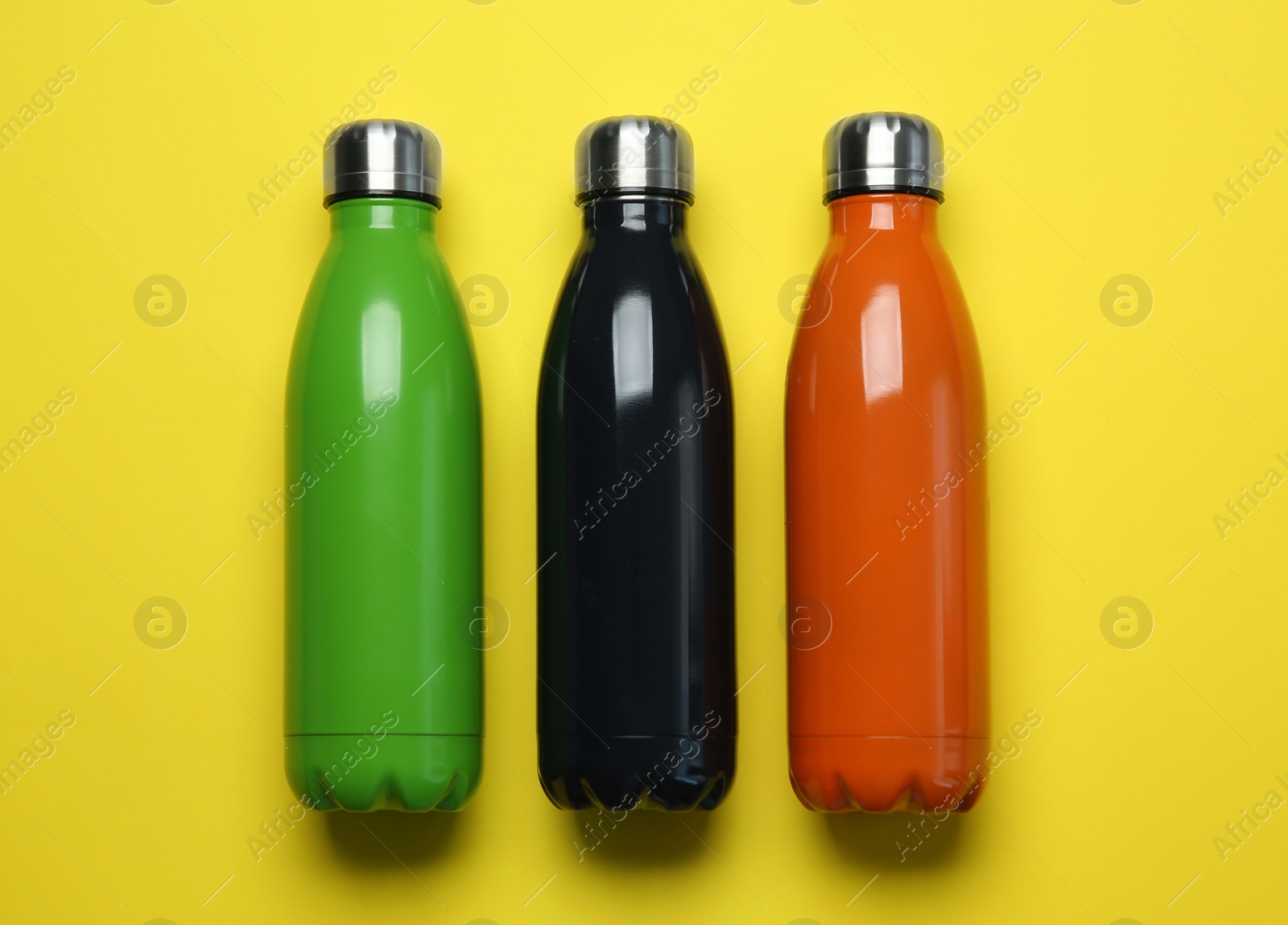 Photo of Different thermo bottles on yellow background, flat lay