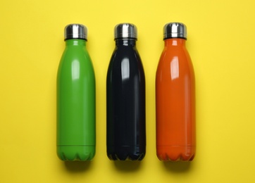 Photo of Different thermo bottles on yellow background, flat lay