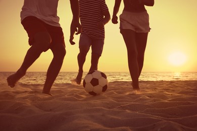 Friends playing football on beach at sunset, closeup