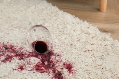 Photo of Overturned glass and spilled red wine on white carpet, space for text