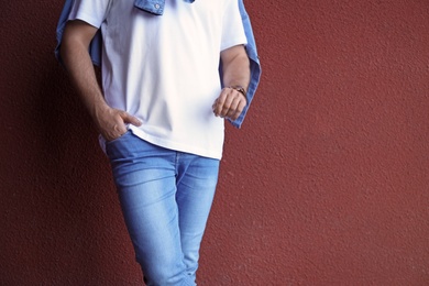 Young hipster man in stylish jeans posing near color wall