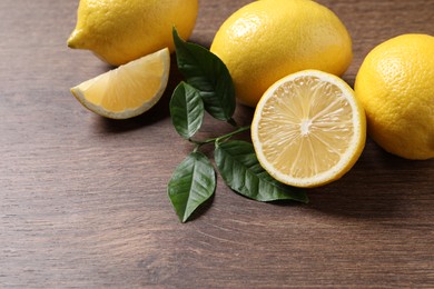 Photo of Fresh lemons and green leaves on wooden table, closeup