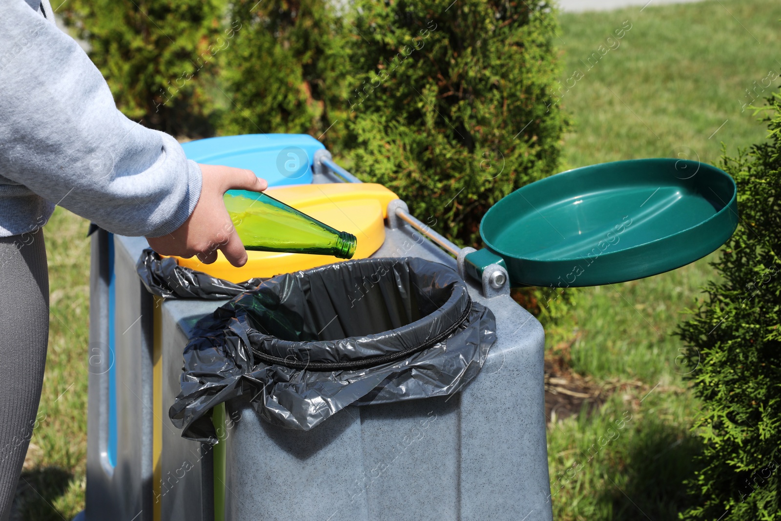 Photo of Woman throwing glass bottle in bin outdoors, closeup. Recycling concept