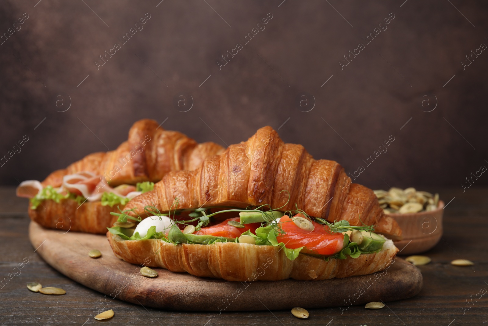 Photo of Delicious croissants with salmon and pumpkin seeds on wooden table