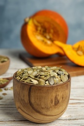 Photo of Bowl of raw pumpkin seeds on white wooden table. Space for text