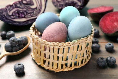 Photo of Colorful Easter eggs painted with natural dyes in wicker bowl on wooden table, closeup