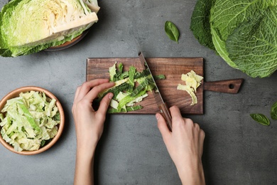 Photo of Woman cutting savoy cabbage on wooden board at table, top view