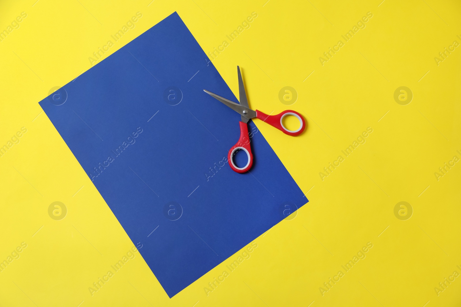 Photo of Red scissors and blue paper on yellow background, top view. Space for text