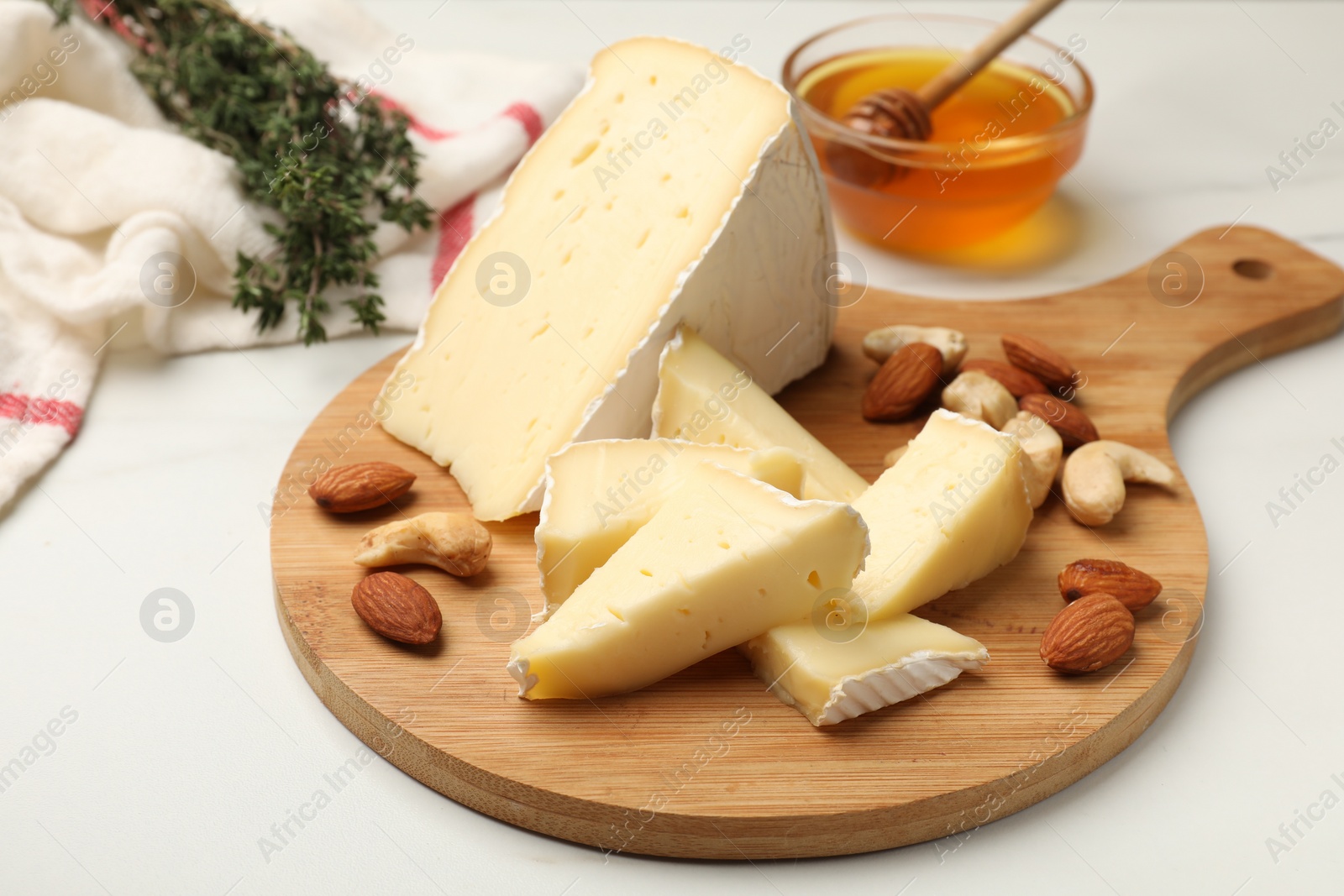 Photo of Tasty Camembert cheese with honey and nuts on white table