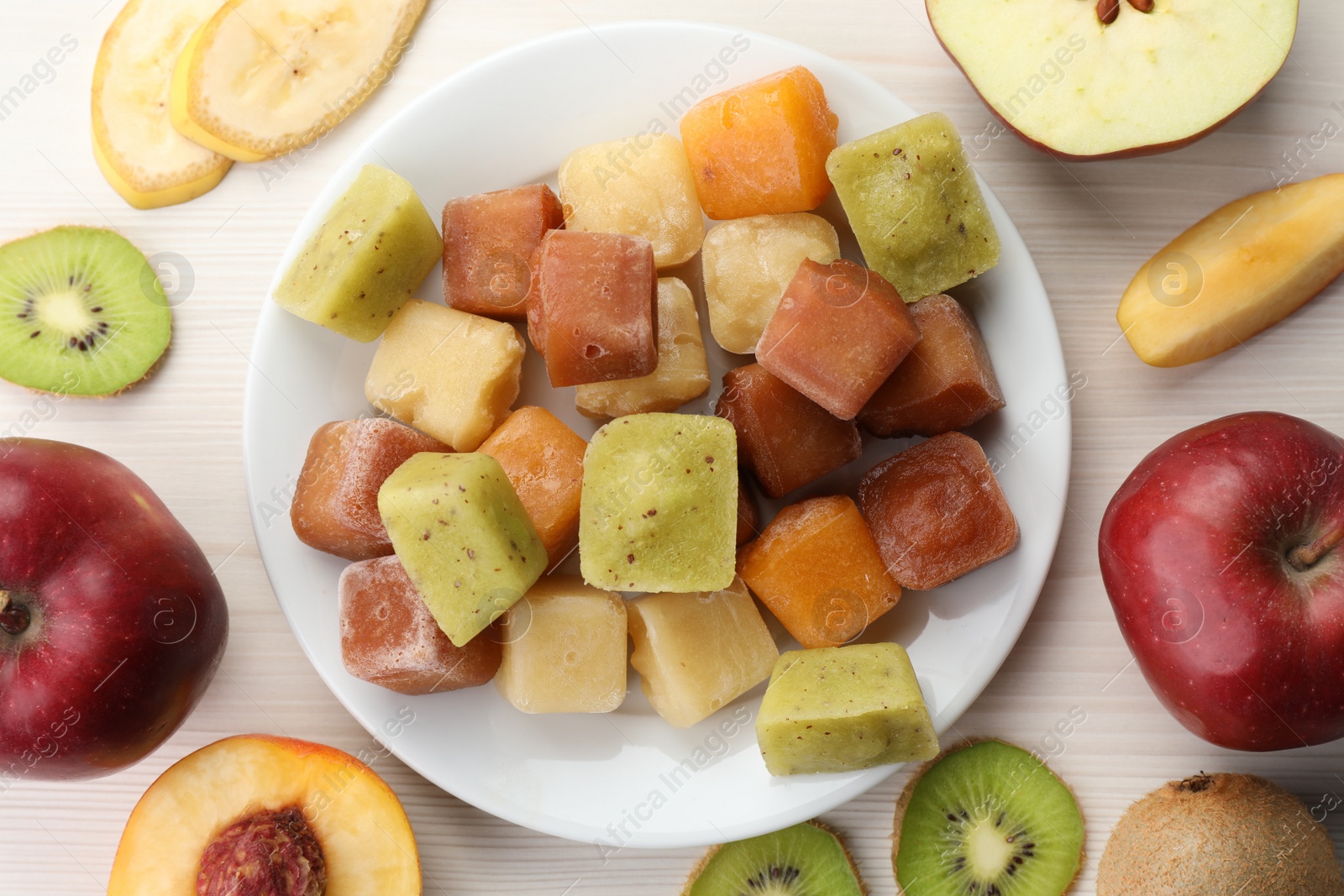 Photo of Different frozen fruit puree cubes and ingredients on white wooden table, flat lay