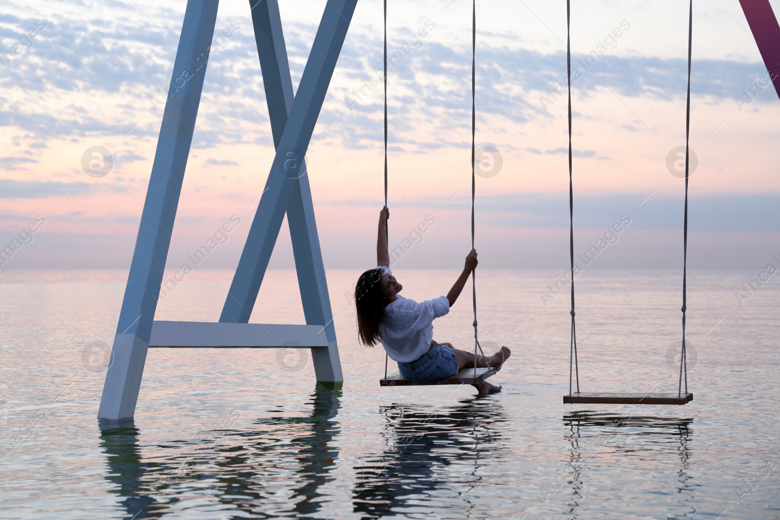 Photo of Young woman enjoying sunrise on swing over water