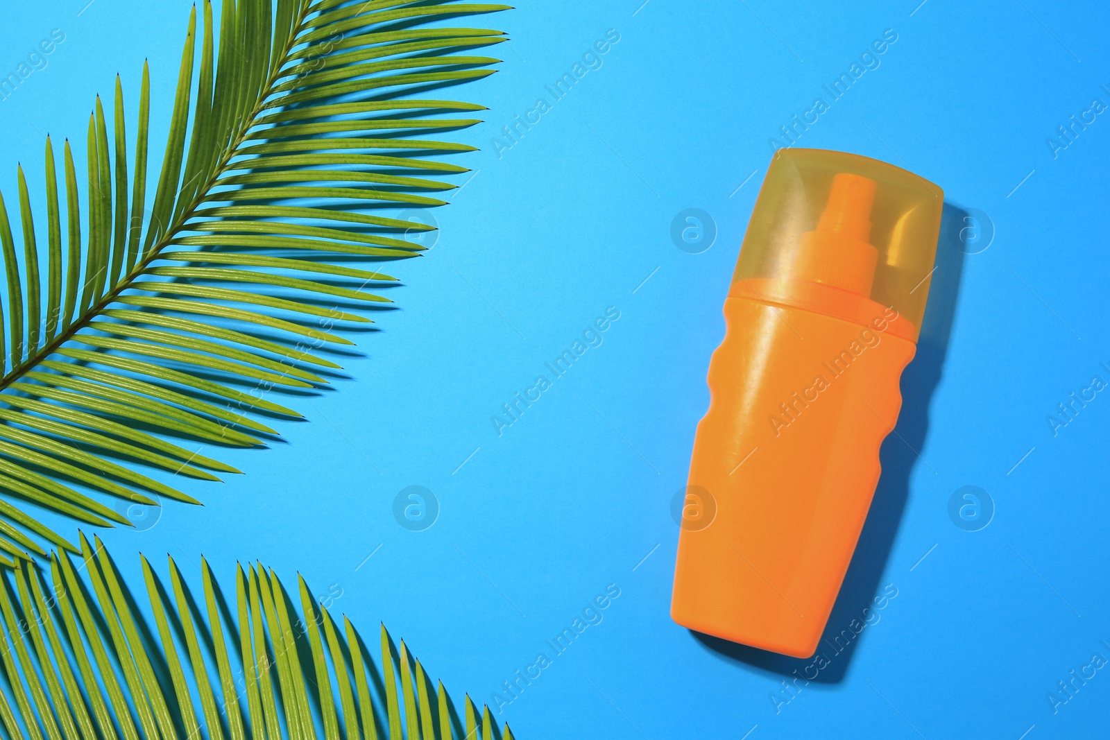 Photo of Sunscreen and tropical leaves on light blue background, flat lay and space for text. Sun protection care