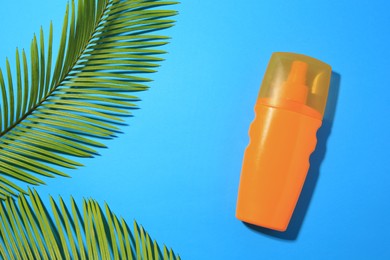 Photo of Sunscreen and tropical leaves on light blue background, flat lay and space for text. Sun protection care