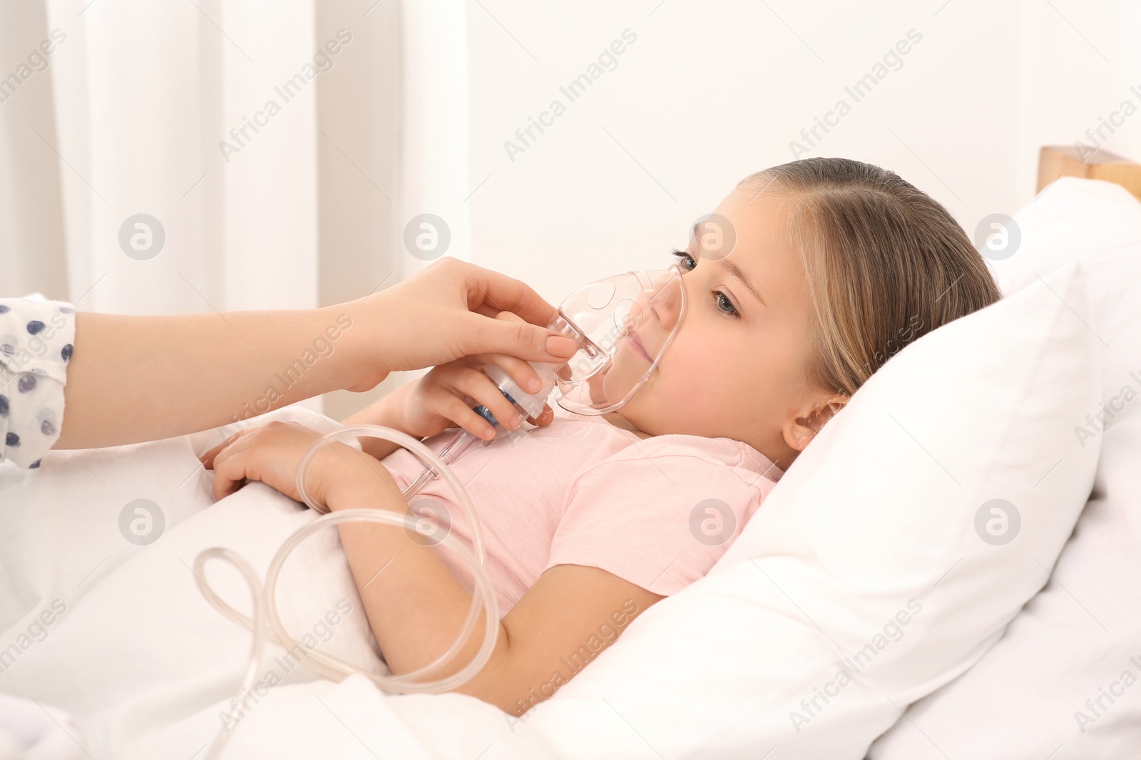 Photo of Mother helping her sick daughter with nebulizer inhalation in bedroom