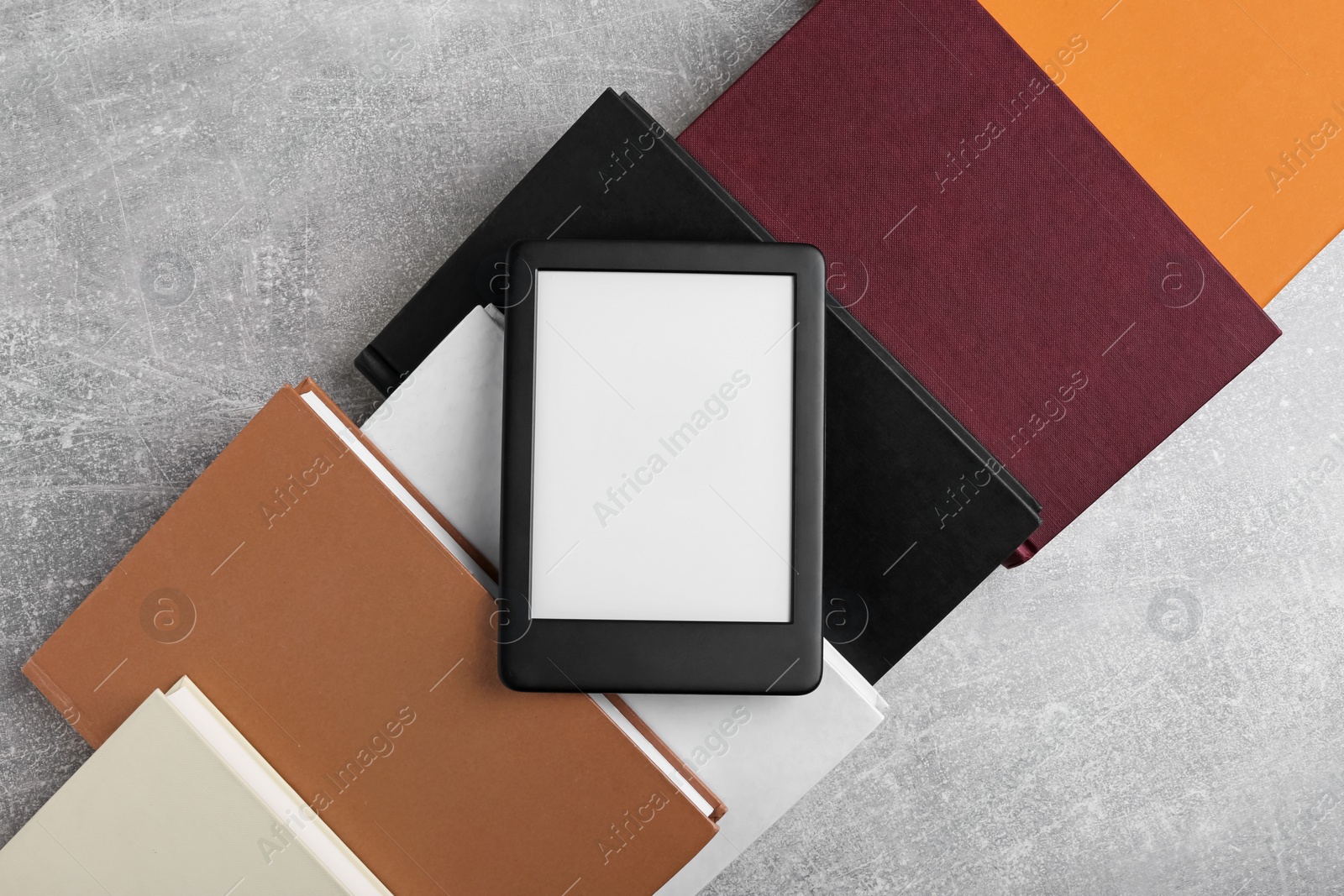 Photo of Portable e-book reader on hardcover books on grey textured table, flat lay