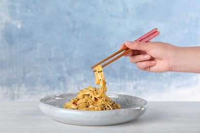 Woman eating cooked Asian noodles with chopsticks at table against color background, closeup