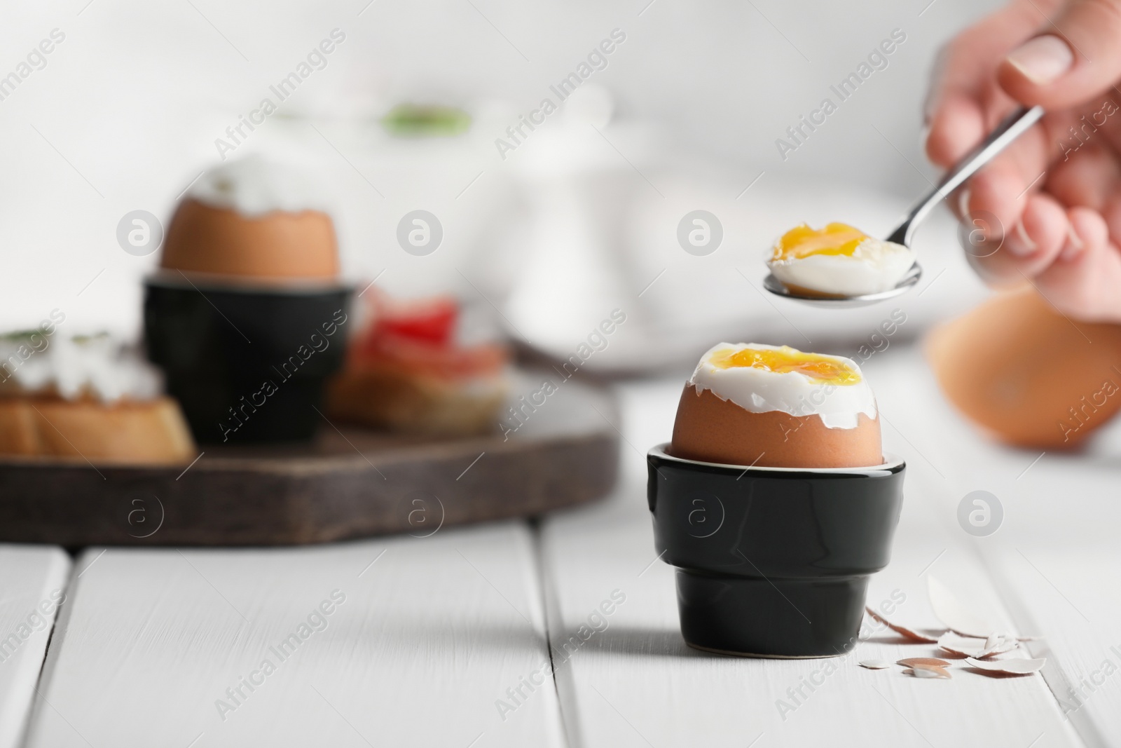 Photo of Woman eating fresh soft boiled egg at white wooden table, closeup. Space for text