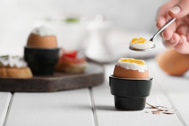 Woman eating fresh soft boiled egg at white wooden table, closeup. Space for text