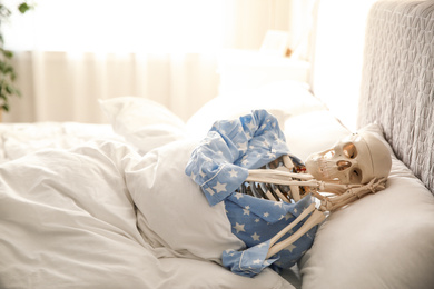 Human skeleton in pajamas lying on bed indoors