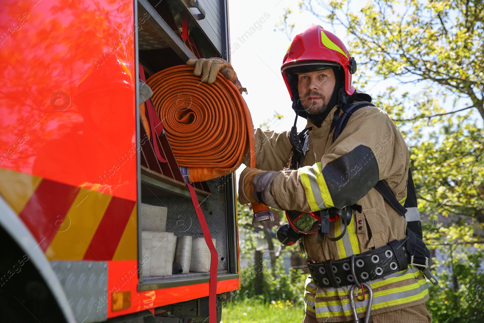 Photo of Firefighter in uniform with fire hose near truck outdoors