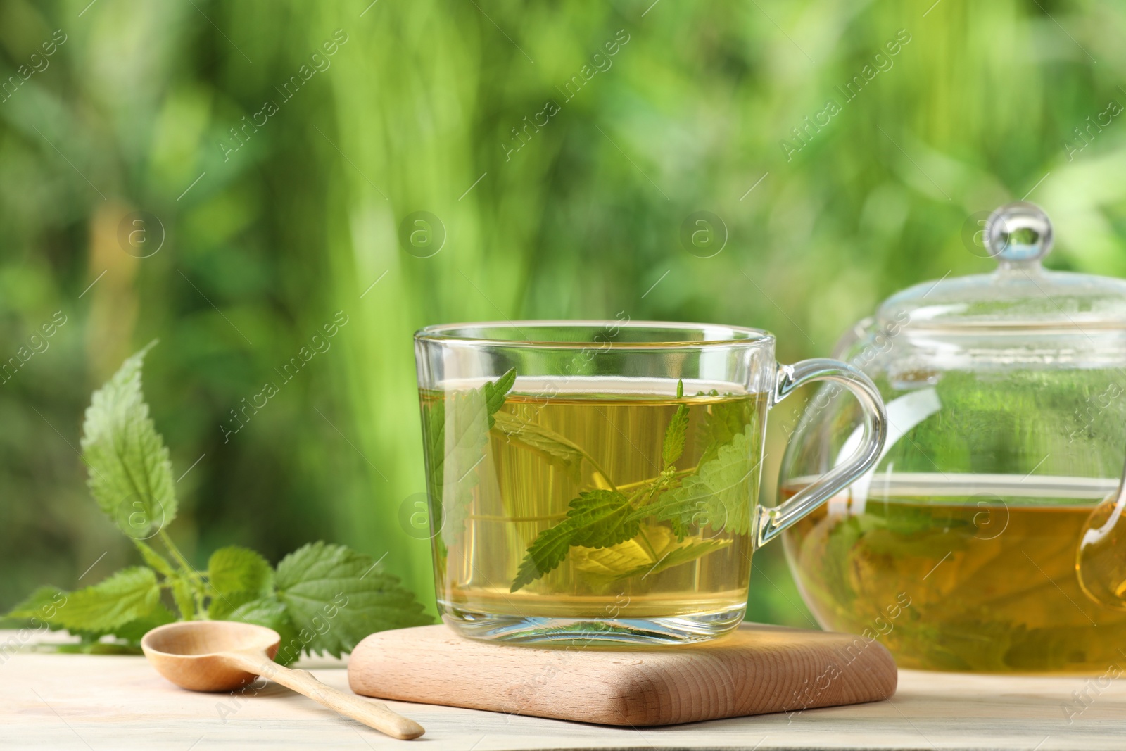 Photo of Aromatic nettle tea and green leaves on table outdoors