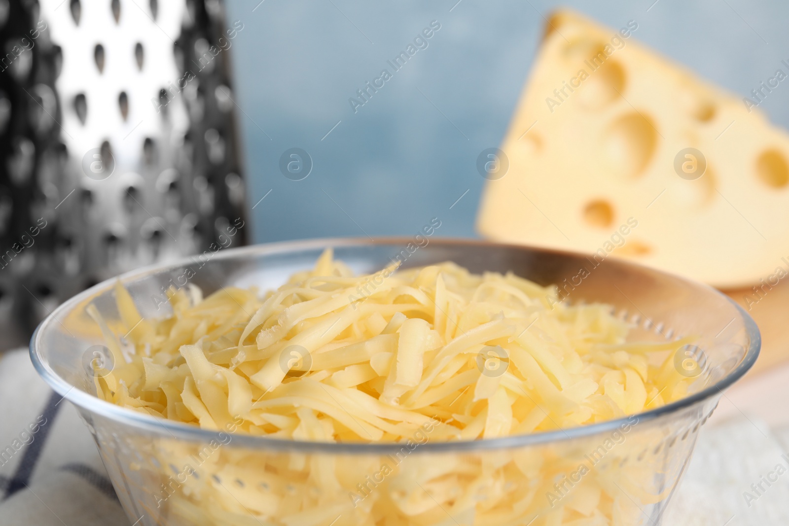 Photo of Delicious grated cheese in glass bowl on table, closeup