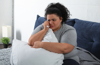 Photo of Depressed overweight woman crying while hugging pillow on bed