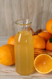 Many ripe oranges and fresh juice on light wooden table