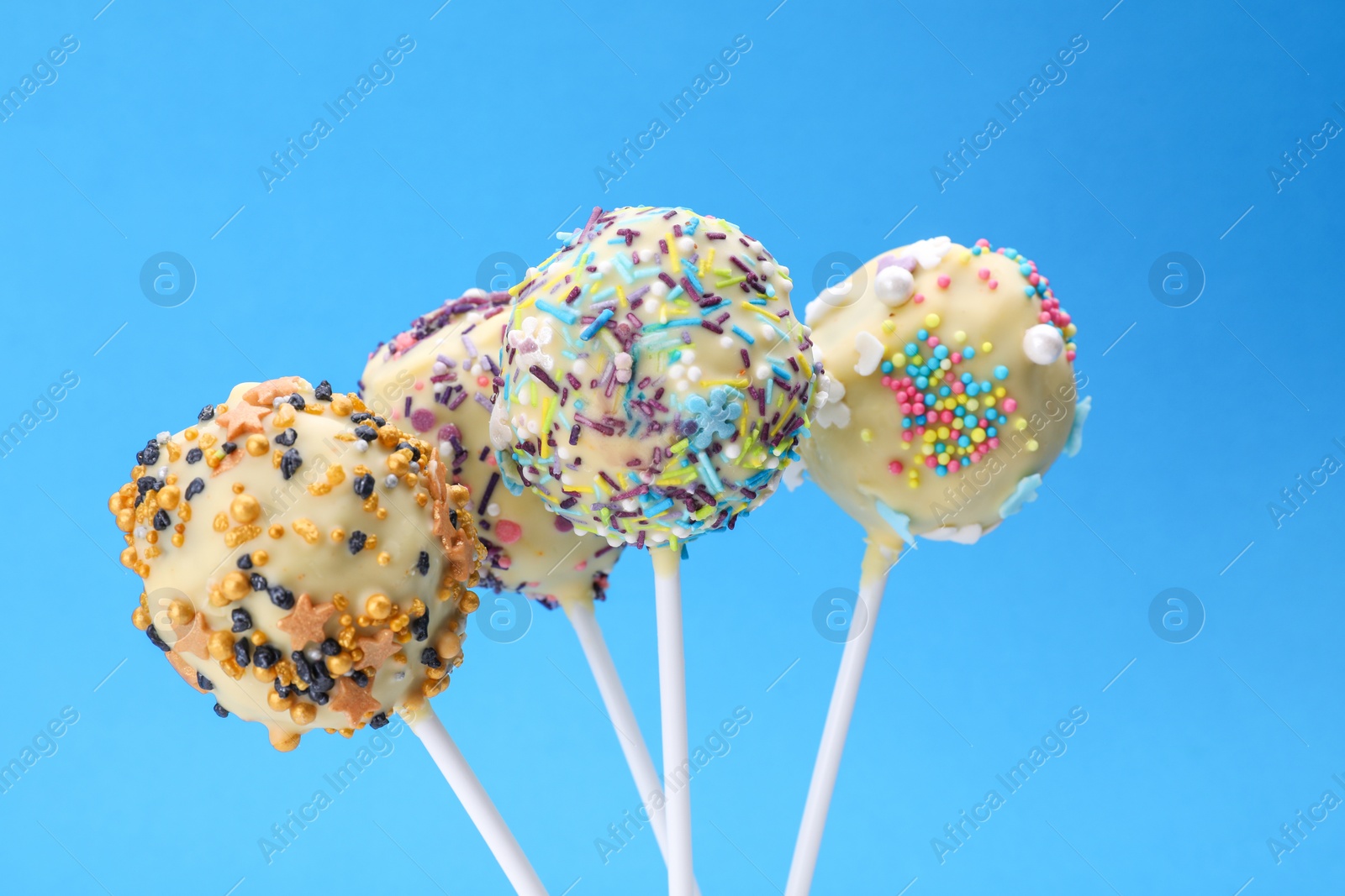 Photo of Sweet cake pops decorated with sprinkles on blue background, closeup. Delicious confectionery