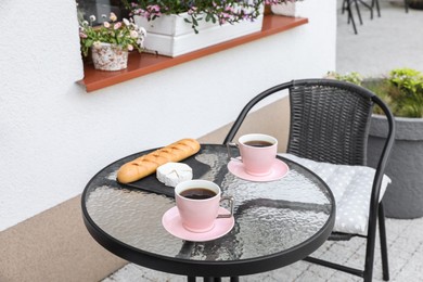 Cups of coffee, bread and cheese on glass table. Relaxing place at outdoor terrace
