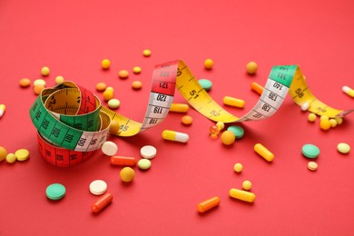 Photo of Many different weight loss pills and measuring tape on red background