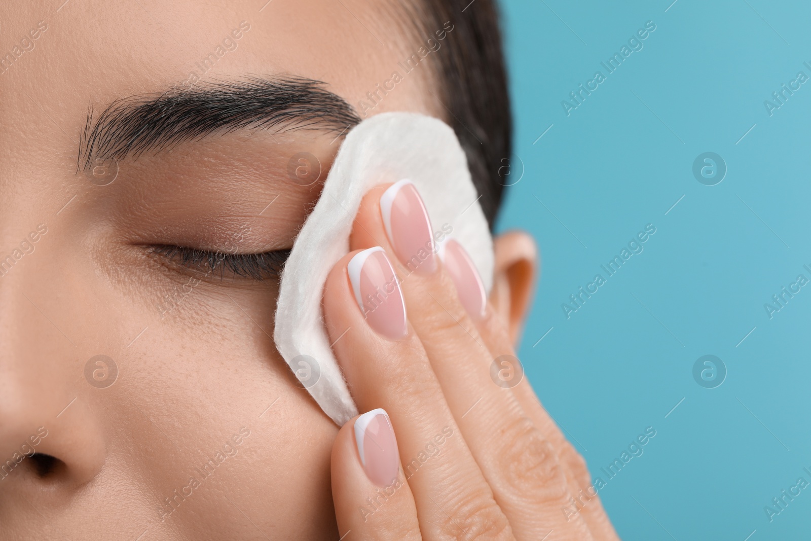 Photo of Beautiful woman removing makeup with cotton pad on light blue background, closeup. Space for text