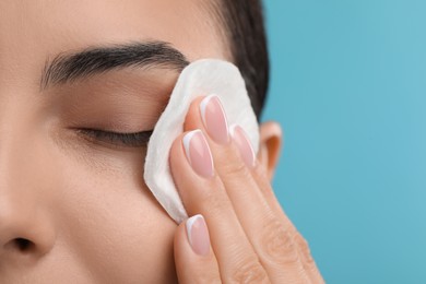 Beautiful woman removing makeup with cotton pad on light blue background, closeup. Space for text