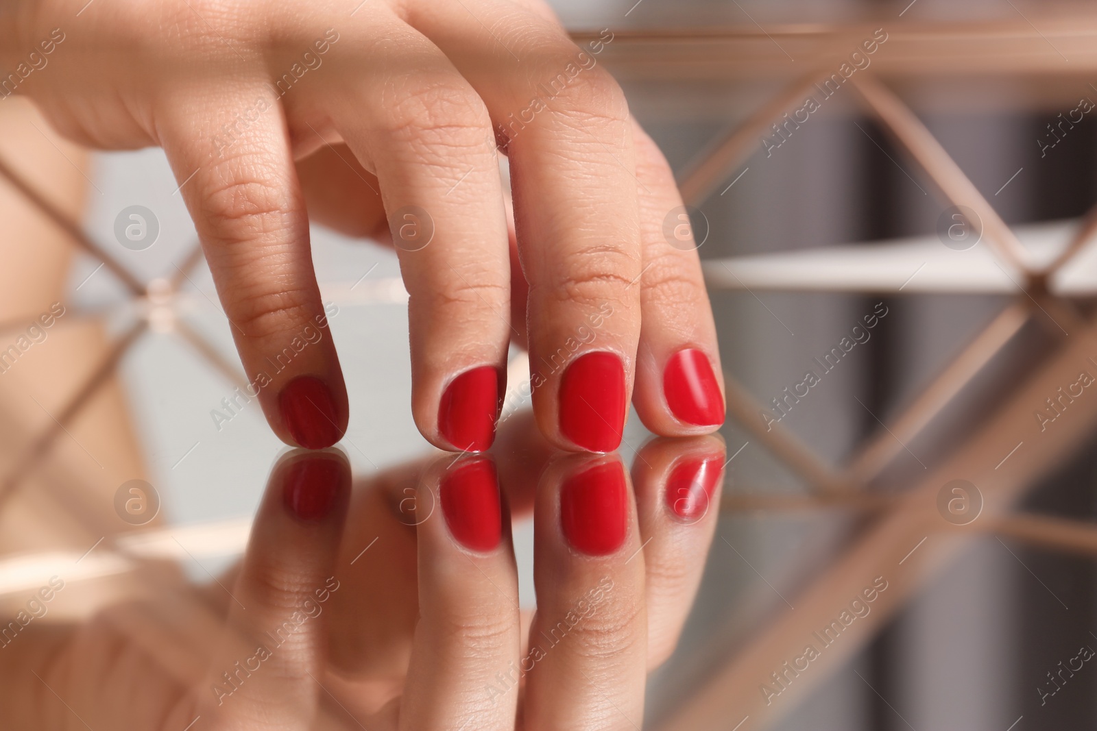 Photo of Woman with red manicure on mirror surface, closeup. Nail polish trends