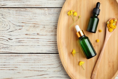 Tray with bottles of essential oil and flowers on wooden table, flat lay. Space for text