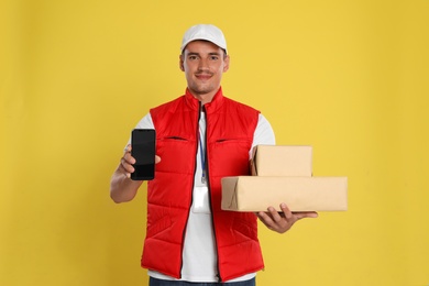 Photo of Happy young courier with mobile phone and parcels on yellow background