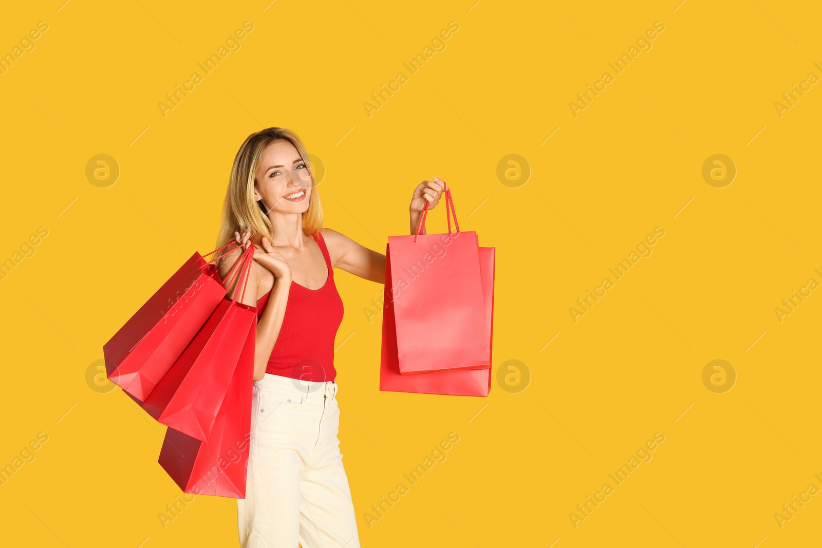 Photo of Happy young woman with shopping bags on yellow background, space for text. Black Friday Sale