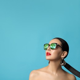Attractive woman in stylish sunglasses on light blue background, space for text. Palm leaves and sky reflecting in lenses