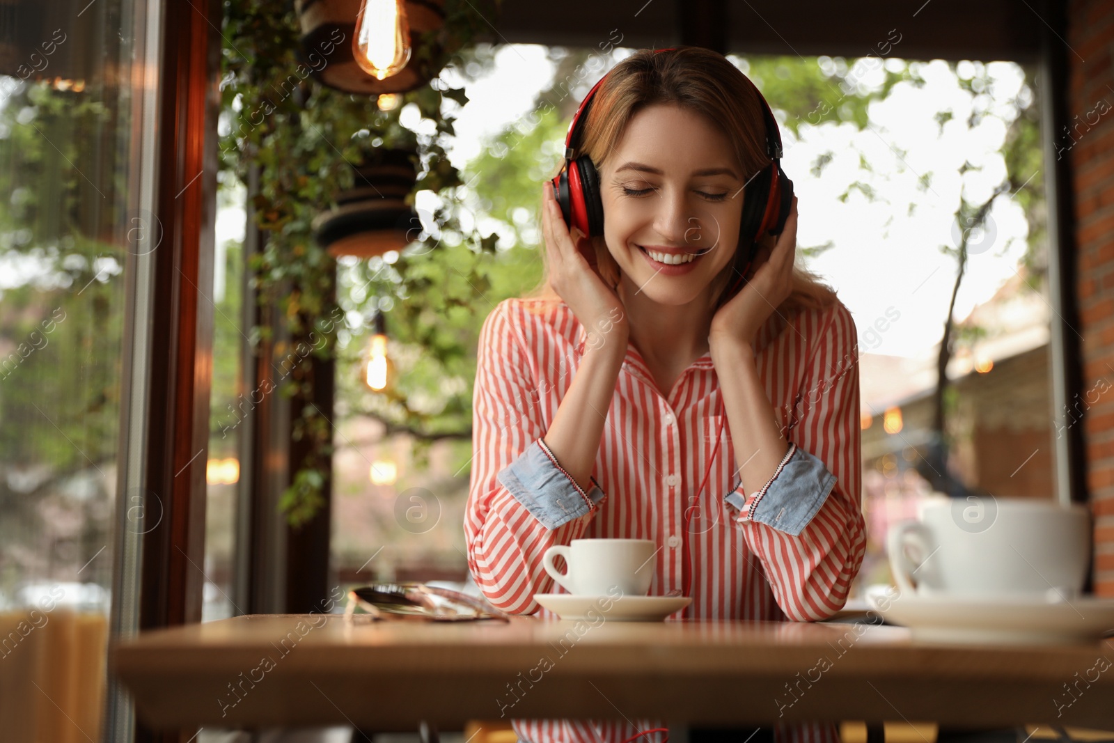 Photo of Young woman with headphones listening to music in cafe