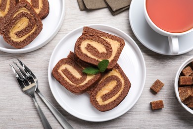 Photo of Tasty chocolate cake roll with cream and mint on light wooden table, flat lay