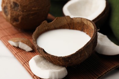 Photo of Delicious vegan milk in coconut and pieces of ripe fruit on white table, closeup