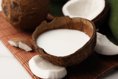 Delicious vegan milk in coconut and pieces of ripe fruit on white table, closeup