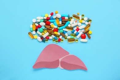 Photo of Paper liver and pills on light blue background, flat lay. Hepatitis treatment