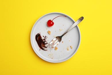 Photo of Dirty plate with food leftovers, fork and canned cherry on yellow background, top view