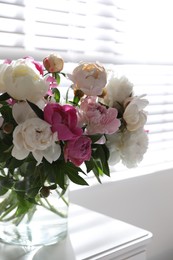 Beautiful peonies in vase on table near window indoors