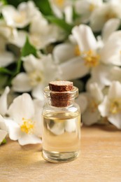 Photo of Jasmine essential oil and fresh flowers on wooden table