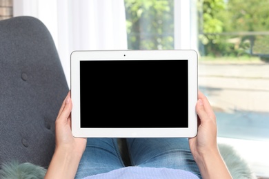 Woman holding tablet with blank screen on blurred background. Mockup for design