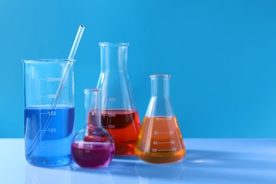Different laboratory glassware with colorful liquids on white table against light blue background. Space for text